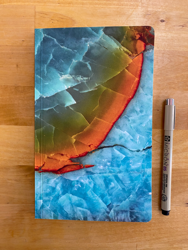 product photo:  notebook with the cover of an abstract macro photo of a mineral showing blues and orange  with pen