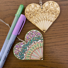 Load image into Gallery viewer, Lay Flat Product Image: 2 Color Your Own Wooden Heart with fan mandala design - one colored in - one uncolored along with a lavender sharpie marker and green gel pen